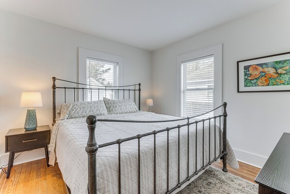 A bedroom with a bed, nightstands, a lamp, and a window with blinds. - Walk to Harbor, Eats & Shops! Greenport Retreat (Greenport)