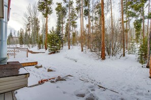 Une forêt enneigée avec une terrasse en bois et une structure métallique.