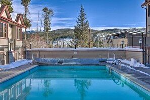 A swimming pool with a view of snow-covered mountains and pine trees. - Heated Pool & Hot Tubs at Dtwn Winter Park Condo! (Winter Park)