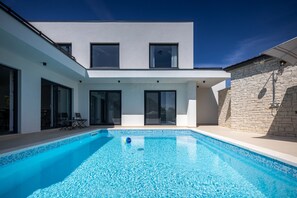 Et moderne hus med swimmingpool, store vinduer og en stenvæg.