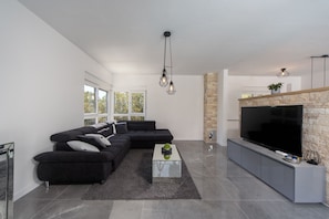 A modern living room with a sectional sofa, a flat-screen TV, and a stone fireplace. - Villa Loto Zadarvillas (Posedarje)
