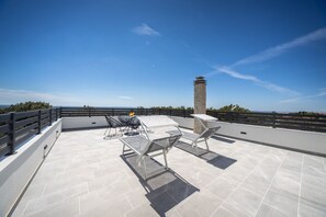 Eine Dachterrasse mit einem Steinkamin, zwei Liegestühlen und einem Tisch.