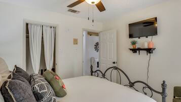 A bedroom with a bed, a ceiling fan, a TV mounted on the wall, and a door leading to another room.