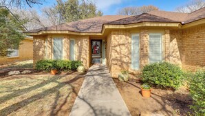 A brick house with a front porch, a pathway leading to the door, and potted plants. - Near Attractions: Family-friendly Lubbock Home! (Lubbock)