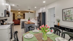 A modern kitchen with white cabinets, a dining table set with plates and a vase of tulips, and a refrigerator. - Near Attractions: Family-friendly Lubbock Home! (Lubbock)