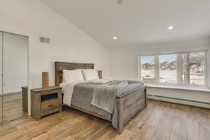 A bedroom with a wooden bed, a nightstand, a mirror, and a window with a view of the outside. - Family Summer Getaway w/ Hot Tub on Lake Hopatcong (Lake Hopatcong)