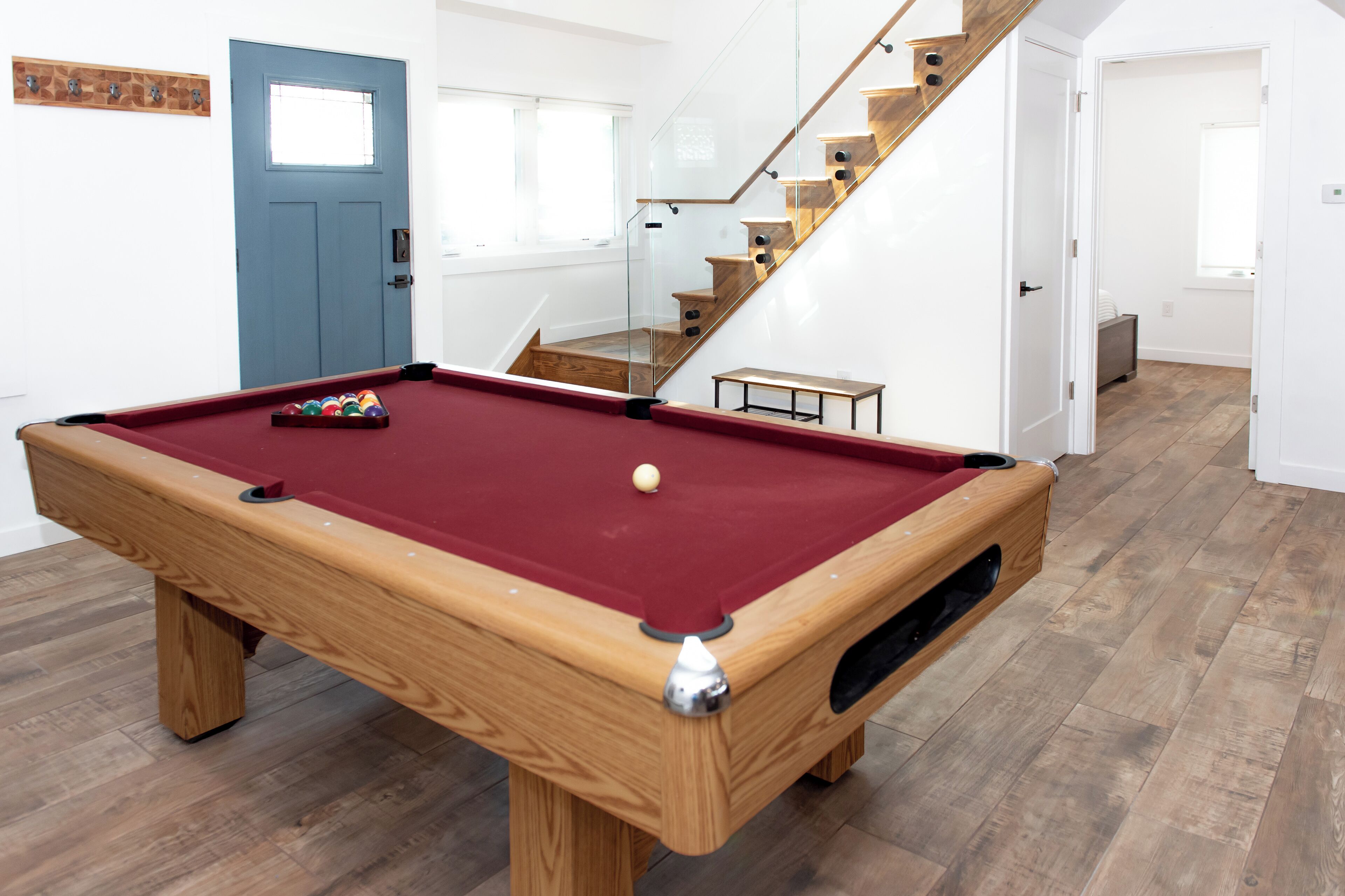 A pool table in a room with wooden flooring, a blue door, and a staircase.
