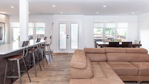 A modern kitchen with a bar area, a large beige sectional sofa, and a dining table with chairs. - Family Summer Getaway w/ Hot Tub on Lake Hopatcong (Lake Hopatcong)