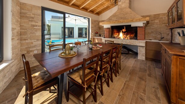 Une cuisine spacieuse avec une cheminée en pierre, des poutres apparentes en bois et une vue sur une piscine.