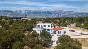 Une maison moderne à deux étages, dotée d’une piscine, entourée d’arbres et avec des montagnes en toile de fond.
