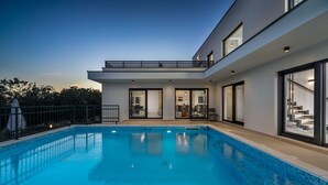 Une maison moderne dotée d’une piscine, de grandes fenêtres et d’un balcon.