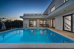 Ein modernes Haus mit Schwimmbad, großen Fenstern und einem Balkon.