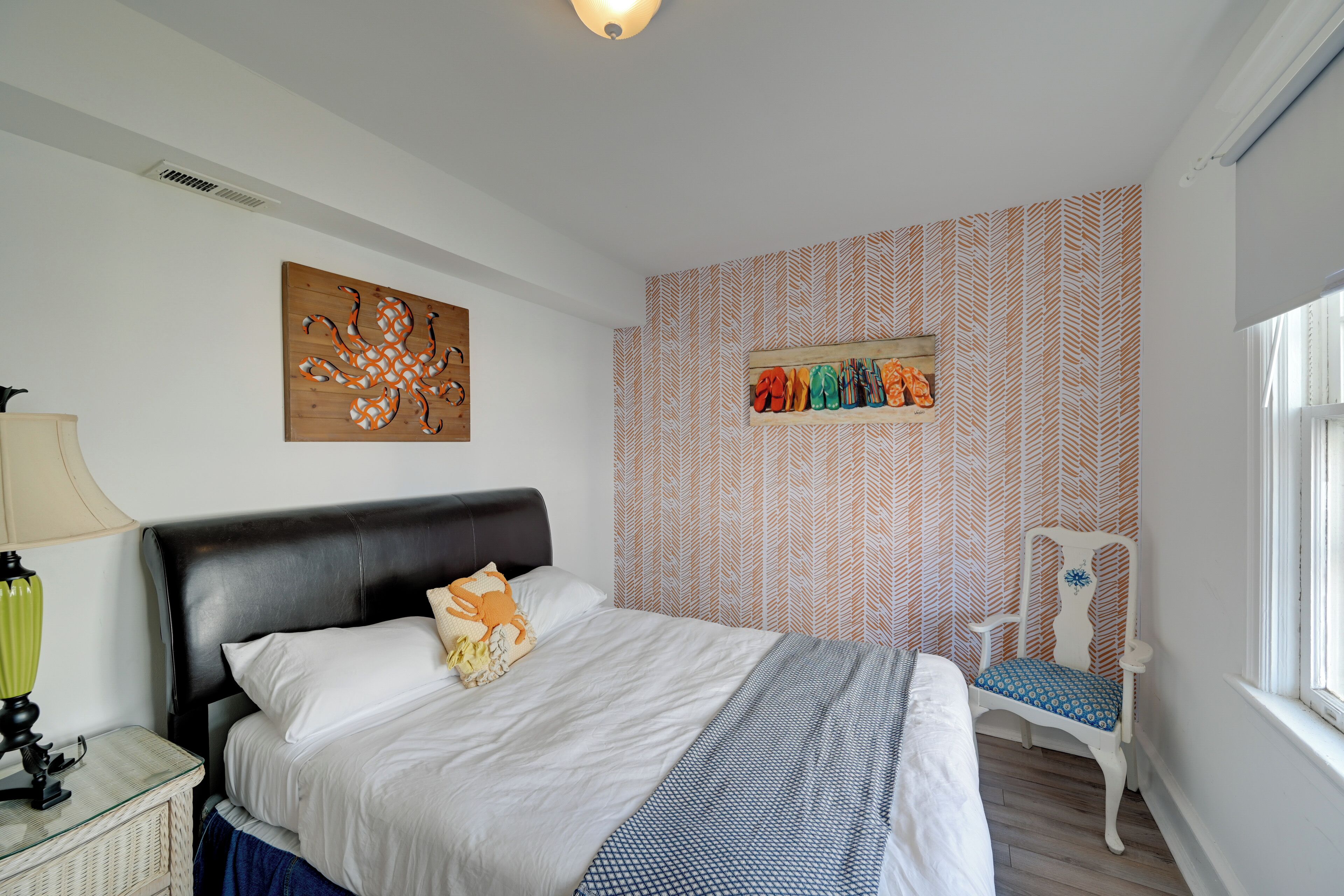 A bedroom with a bed, a chair, a wall art piece, and a shelf with colorful items.