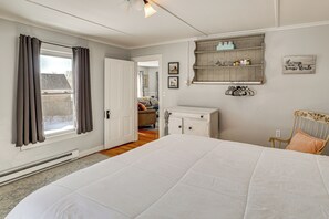 A bedroom with a large bed, a dresser, a chair, a shelf with items, and a door leading to another room. - Easy Beach Access! New London Apt w/ Kitchenette (New London)