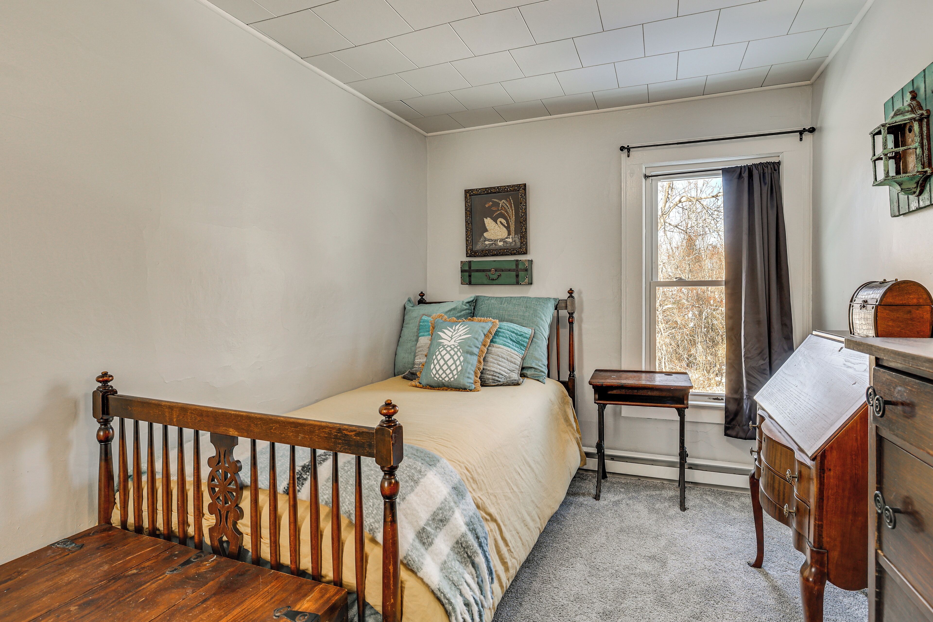 A bedroom with a wooden bed, a nightstand, a dresser, a window with curtains, and a wall-mounted shelf.