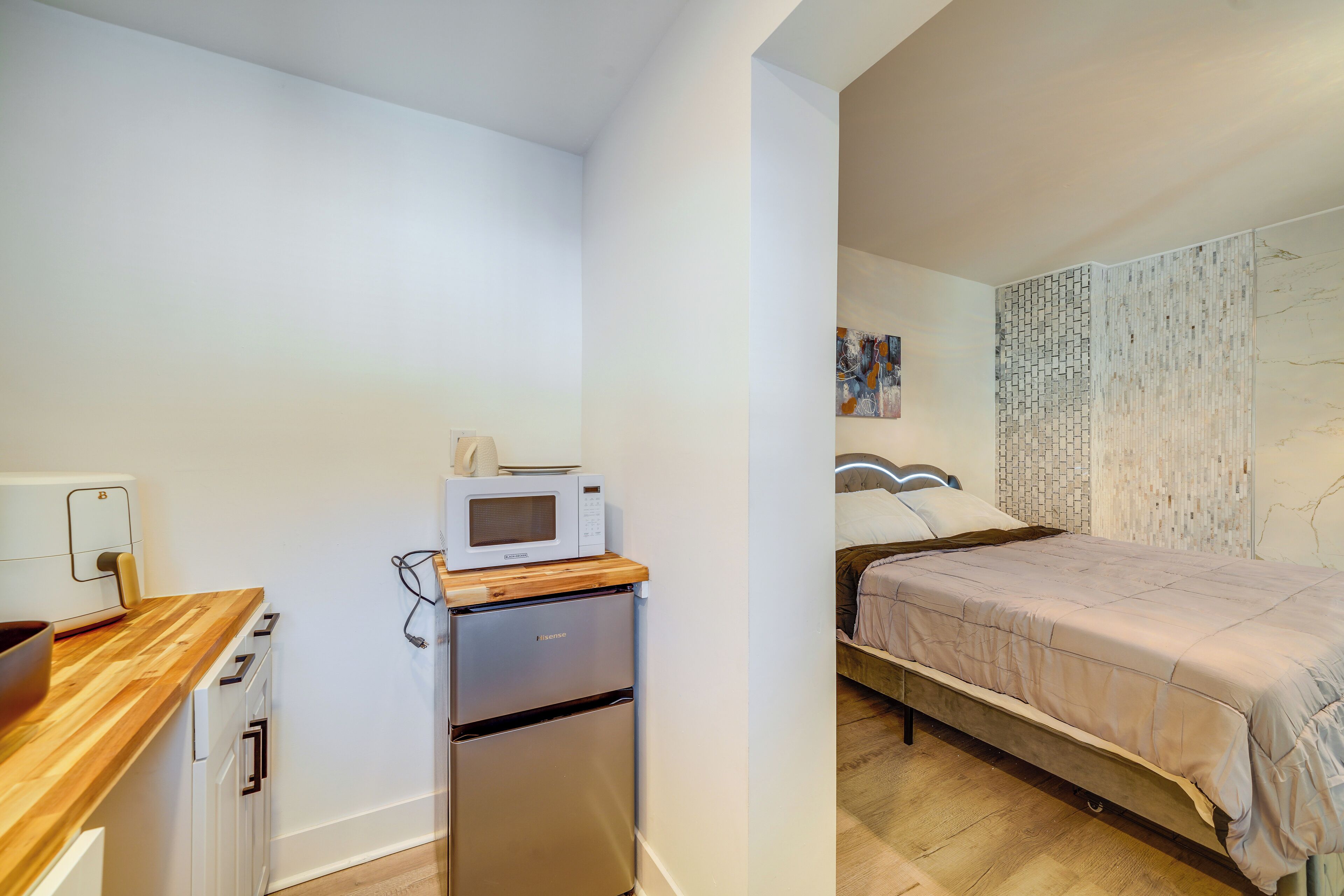 A compact room with a kitchenette, a bed with a headboard, and a wall-mounted artwork.