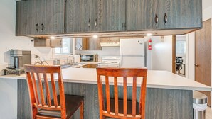 A kitchen with wooden cabinets, a white countertop, a stove, a microwave, and two wooden chairs. - Near Mcnary Dam! Pet-friendly Condo on Golf Course (Umatilla)
