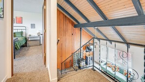 A room with a wooden ceiling, a staircase, a green sofa, and a bed with a green blanket. - Near Mcnary Dam! Pet-friendly Condo on Golf Course (Umatilla)