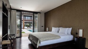 Een moderne hotelkamer met een groot bed, een zithoek met een fauteuil en uitzicht op een zwembad en terras.