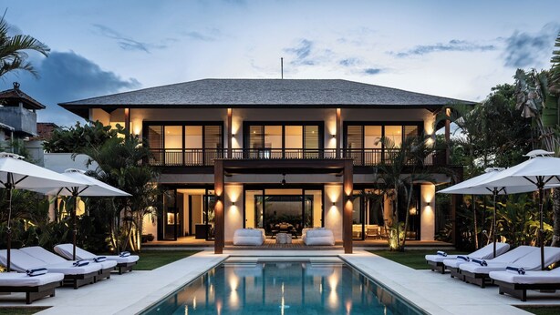 Een modern huis met twee verdiepingen, een zwembad, ligbedden en parasols.