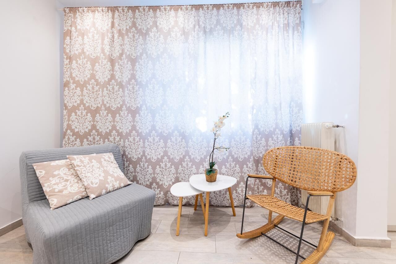 A cozy room with a grey sofa, a wicker chair, a small white table, and a decorative plant.