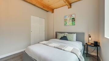 A bedroom with a bed, a bedside table with a lamp, a door, and a painting on the wall.