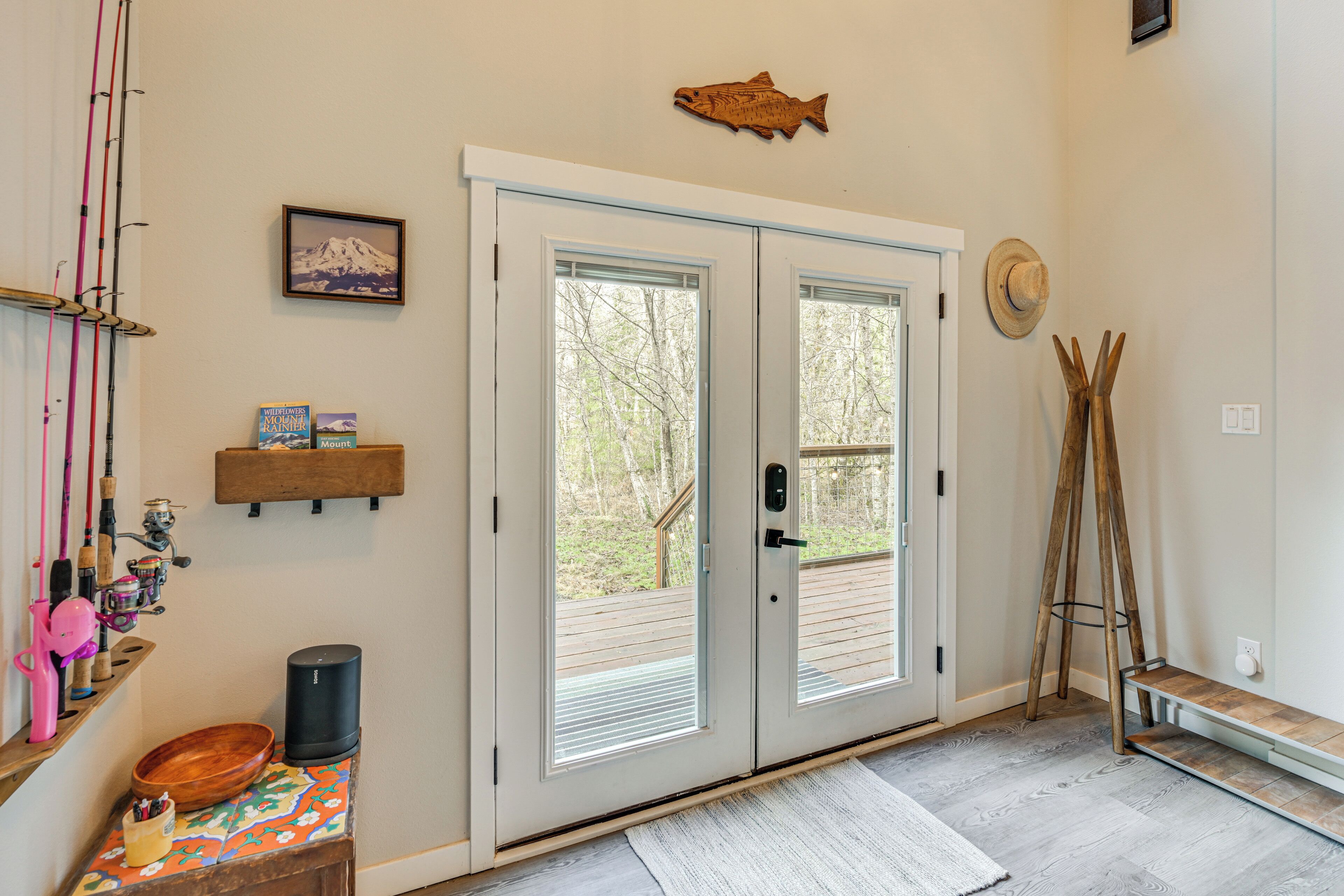 Una habitación con una puerta que da a una terraza exterior, una decoración de pez en la pared, cañas de pescar y una estantería de madera con libros.