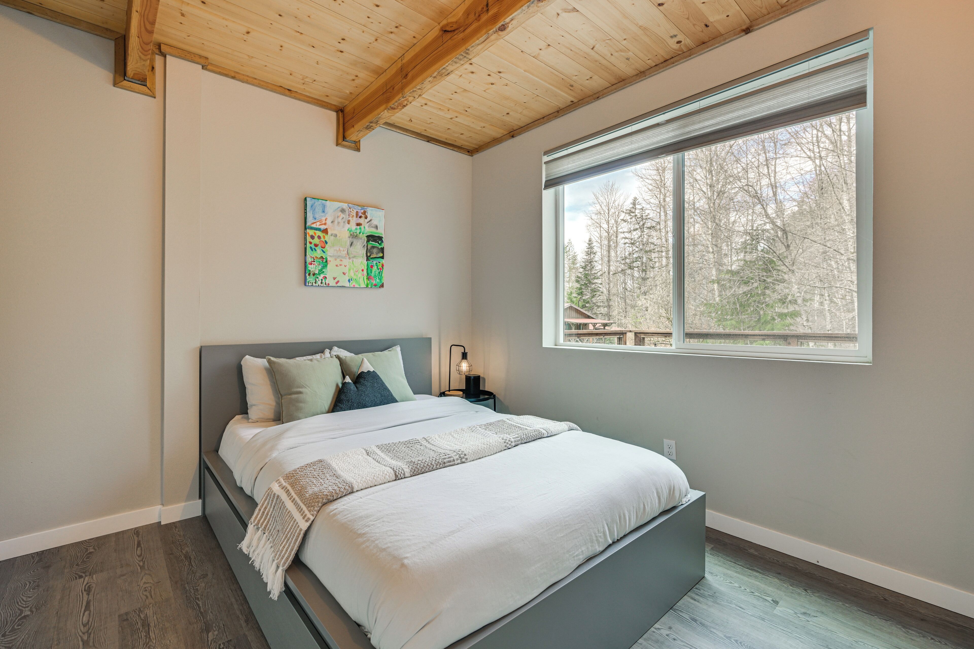 Une chambre à coucher avec un lit, une fenêtre donnant sur des arbres et un tableau accroché au mur.