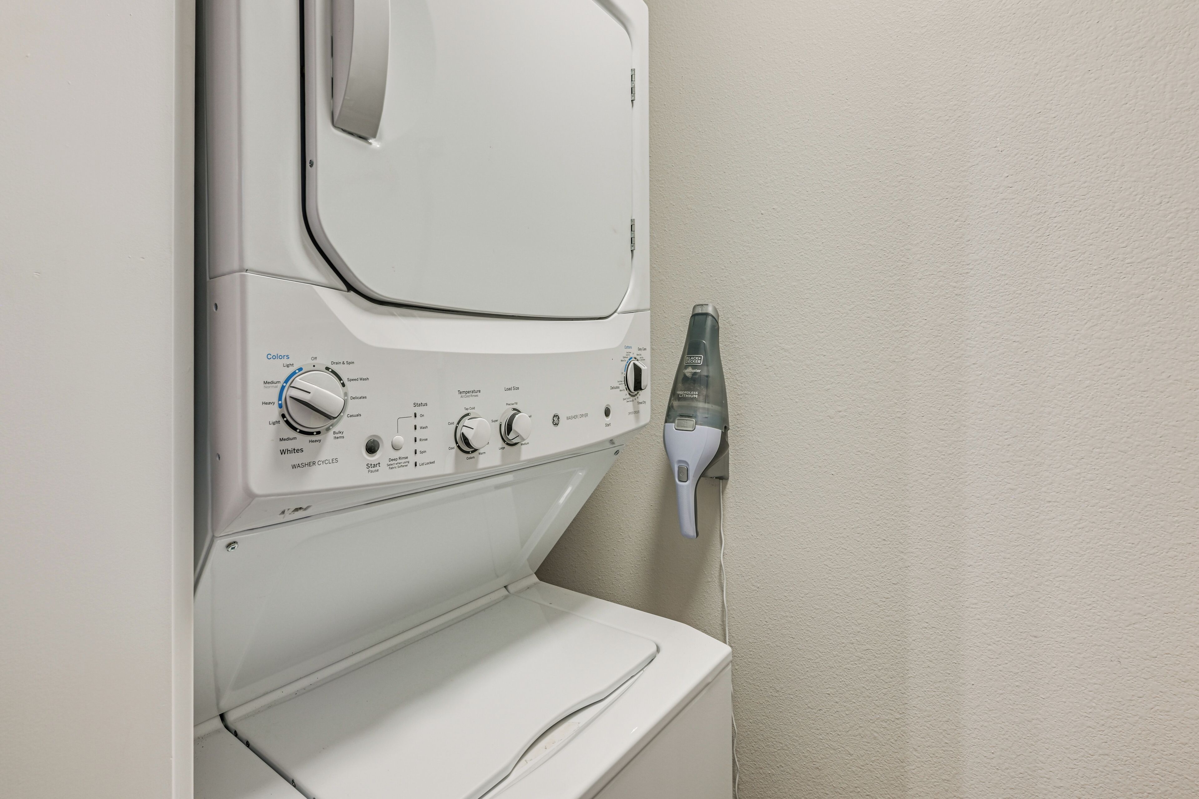 Un lave-linge à chargement frontal doté d’un panneau de commande, d’un robinet d’arrivée d’eau et d’un sèche-linge fixé au mur.