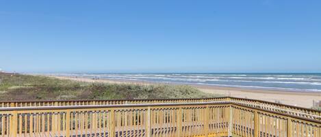 A wooden boardwalk leading to a beach with a clear view of the ocean.