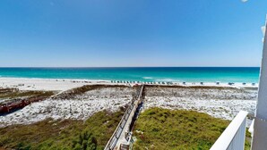 A beach view with a wooden boardwalk leading to the shore, clear skies, and a calm sea. - Destin On The Gulf 506 2 Bedroom Condo (Destin)
