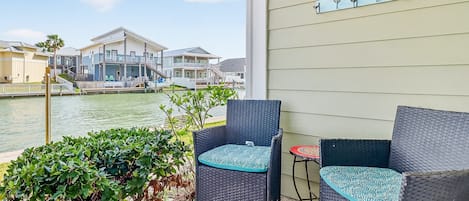 A balcony with wicker furniture, a small table, and a view of houses across a body of water.