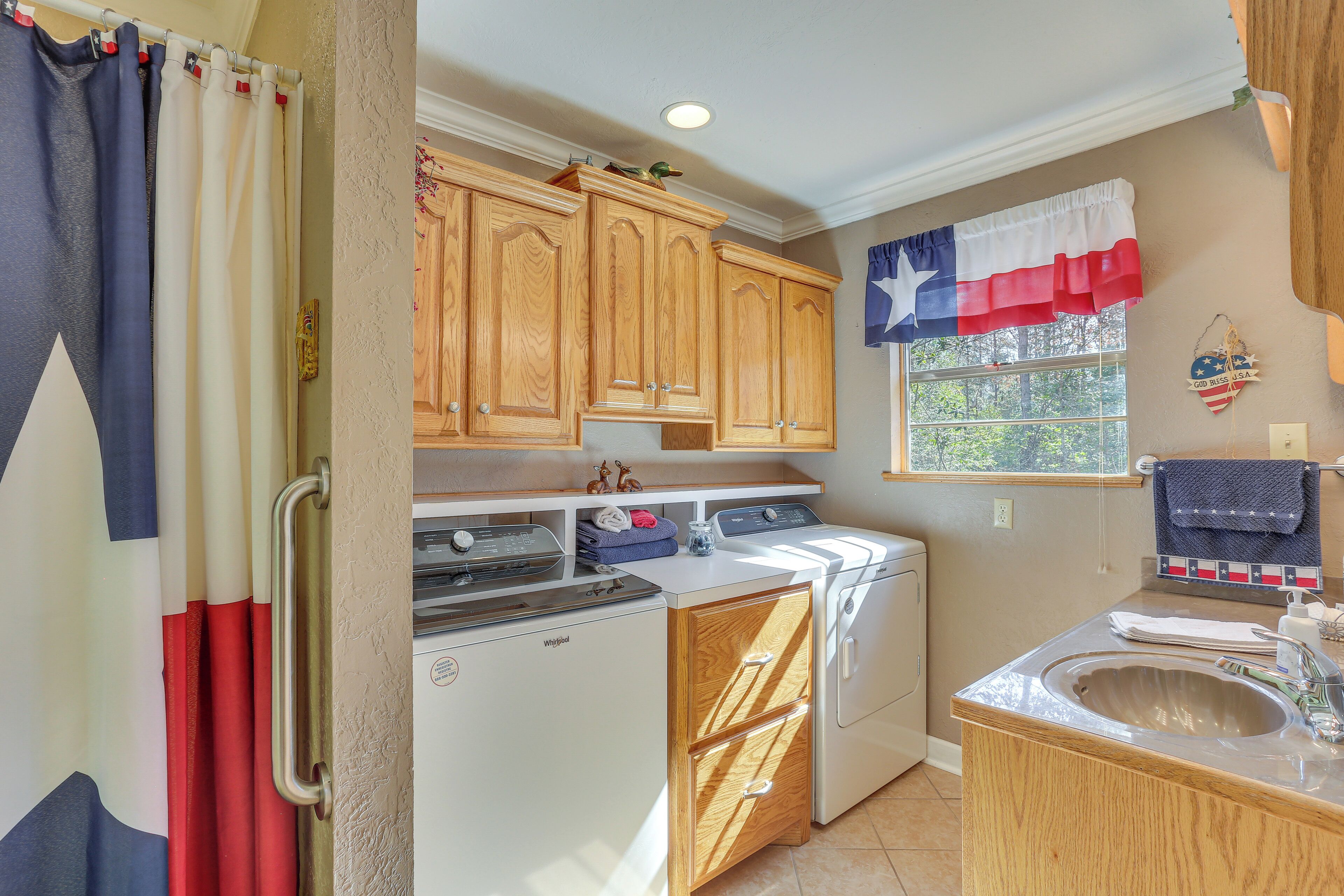 A laundry room with a washer and dryer, wooden cabinets, a window with a view, and a sink with a mirror.