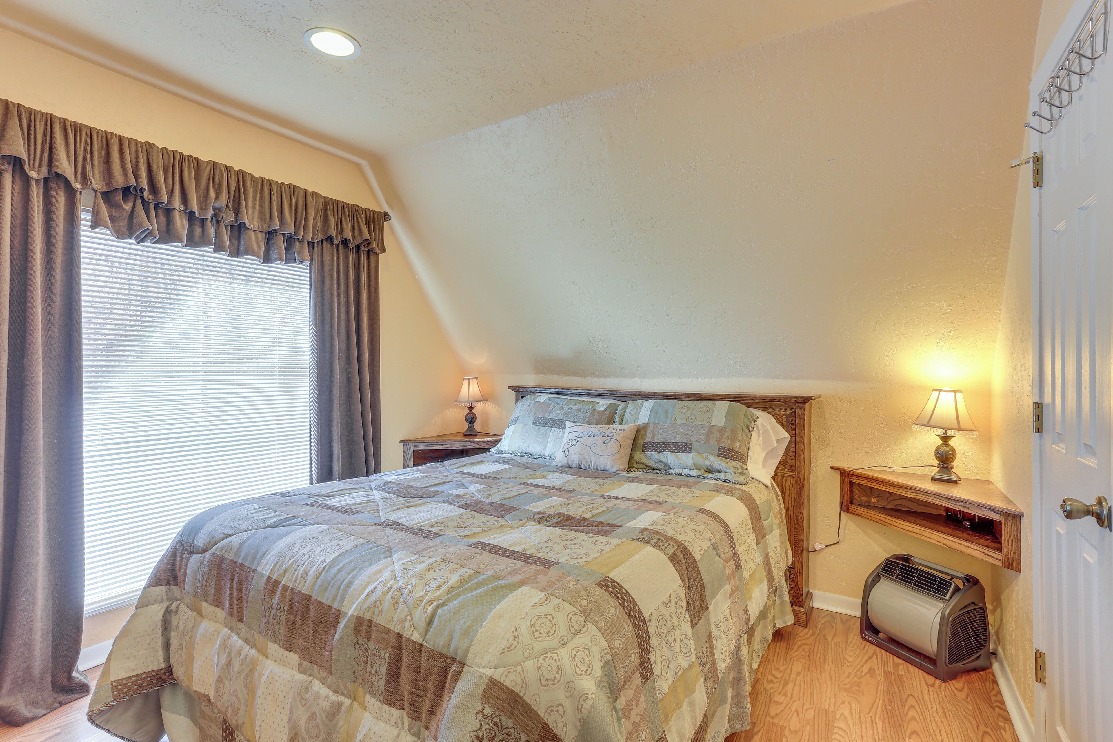 A bedroom with a large bed, two bedside tables with lamps, a heater, and a window with curtains.