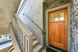 A wooden door with a glass panel, a stone wall, and a concrete staircase with a metal handrail. - Stroll to Shore: Oceanside Condo w/ Hot Tub Access (Oceanside)