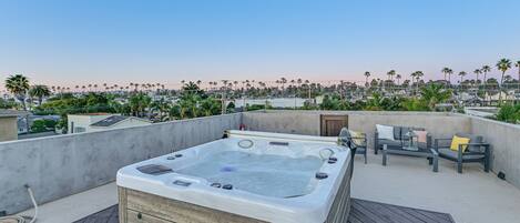 A rooftop terrace with a hot tub, outdoor furniture, and a view of palm trees and buildings.