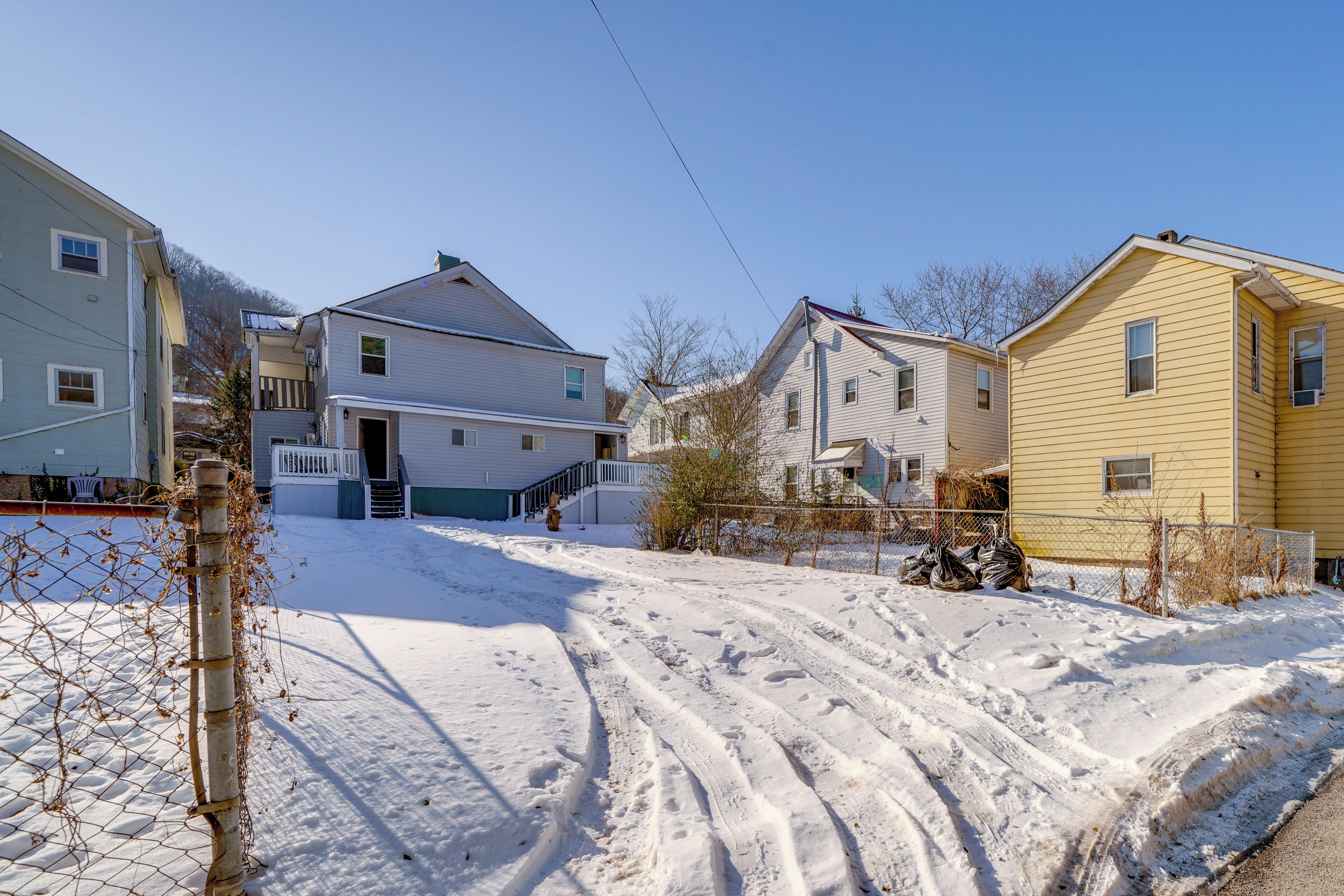 A residential street with houses, a snow-covered driveway, and a fence.