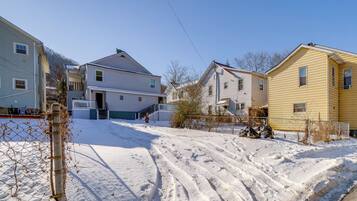 A residential street with houses, a snow-covered driveway, and a fence.