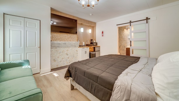Une chambre avec un grand lit, un canapé vert, un coin cuisine et une porte coulissante.