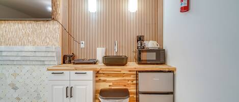Une cuisine compacte dotée d’un plan de travail en bois, d’un four à micro-ondes, d’une machine à café et d’une poubelle.