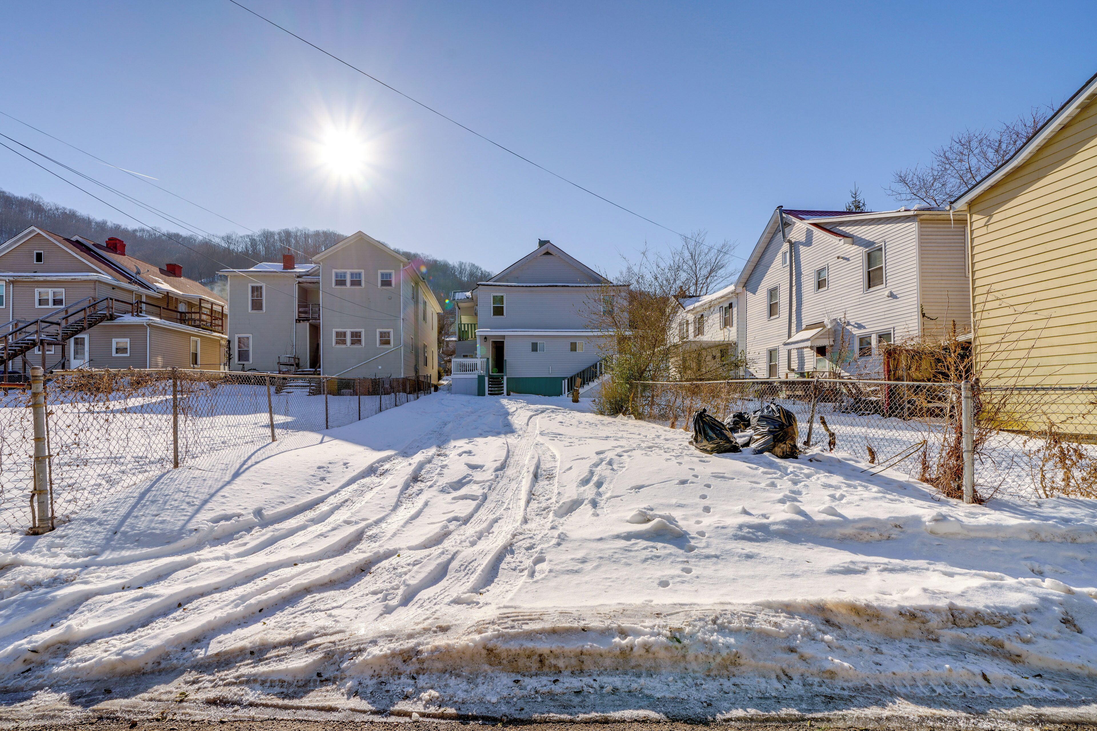 A residential street with houses, a snow-covered path, and a clear sky.