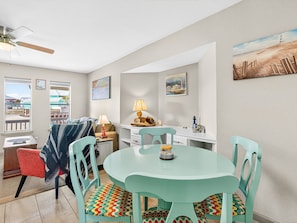 A cozy room with a round table, chairs, a desk, a lamp, and a painting on the wall. - Lighthouse Landing At Kontiki Kc111 1 Bedroom Condo (Rockport)