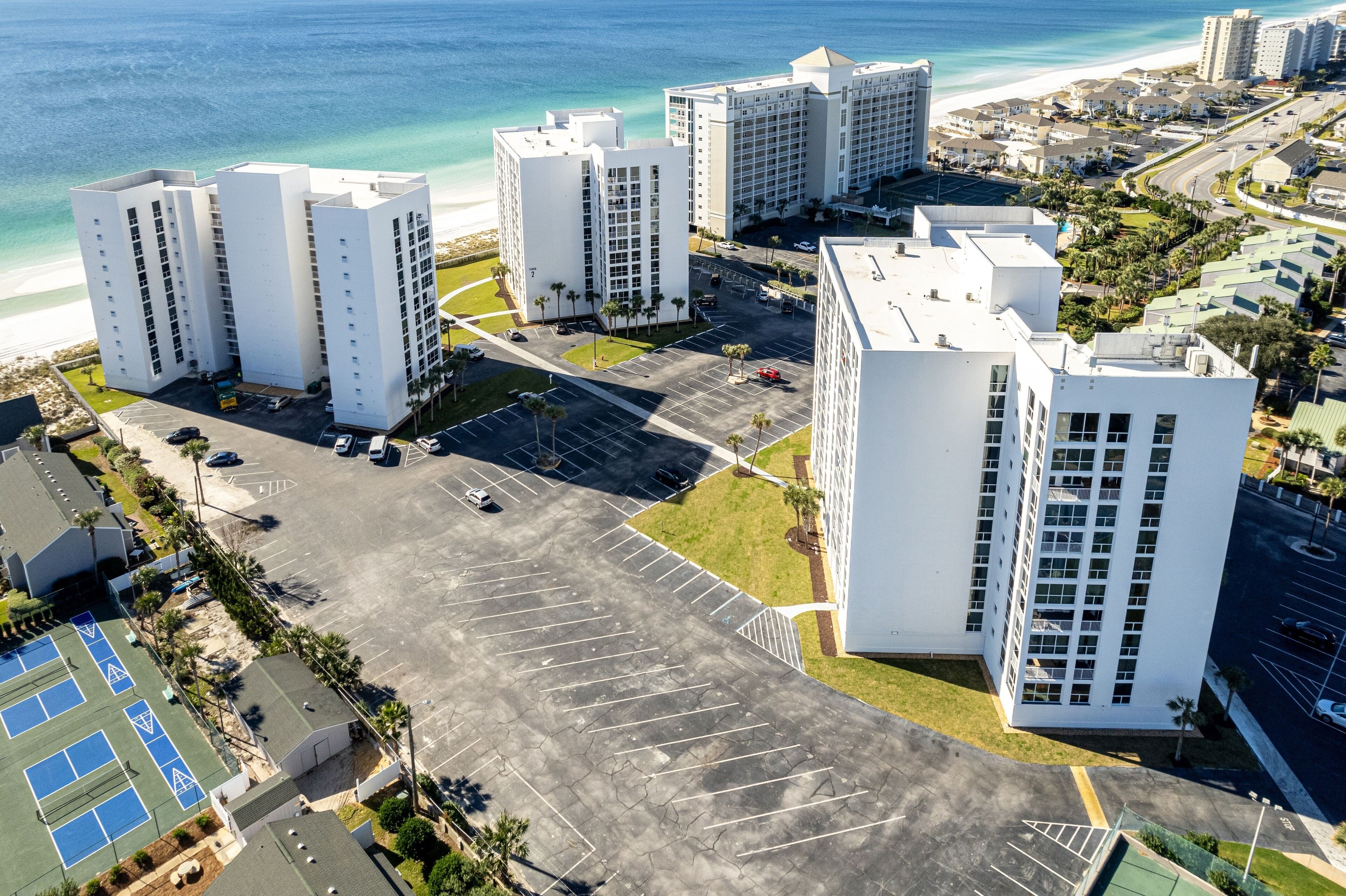 Een hoog hotel met meerdere verdiepingen, een parkeerplaats en uitzicht op het strand.