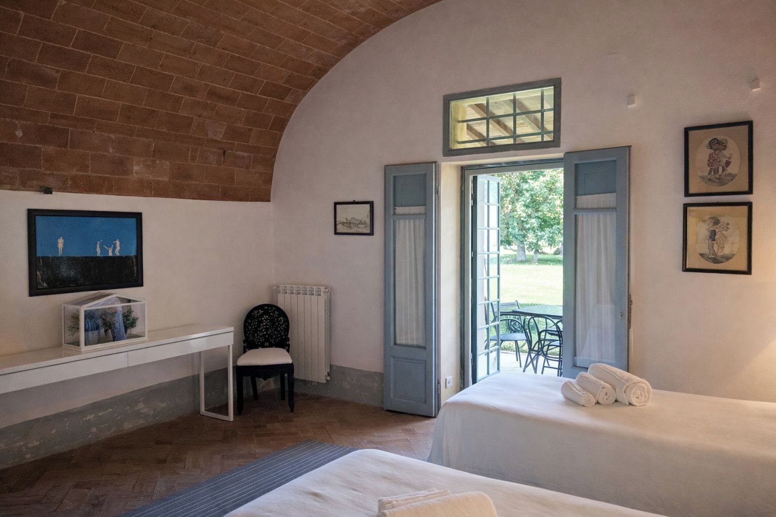 Quarto com duas camas, uma escrivaninha, uma cadeira e janela com vista para o exterior.