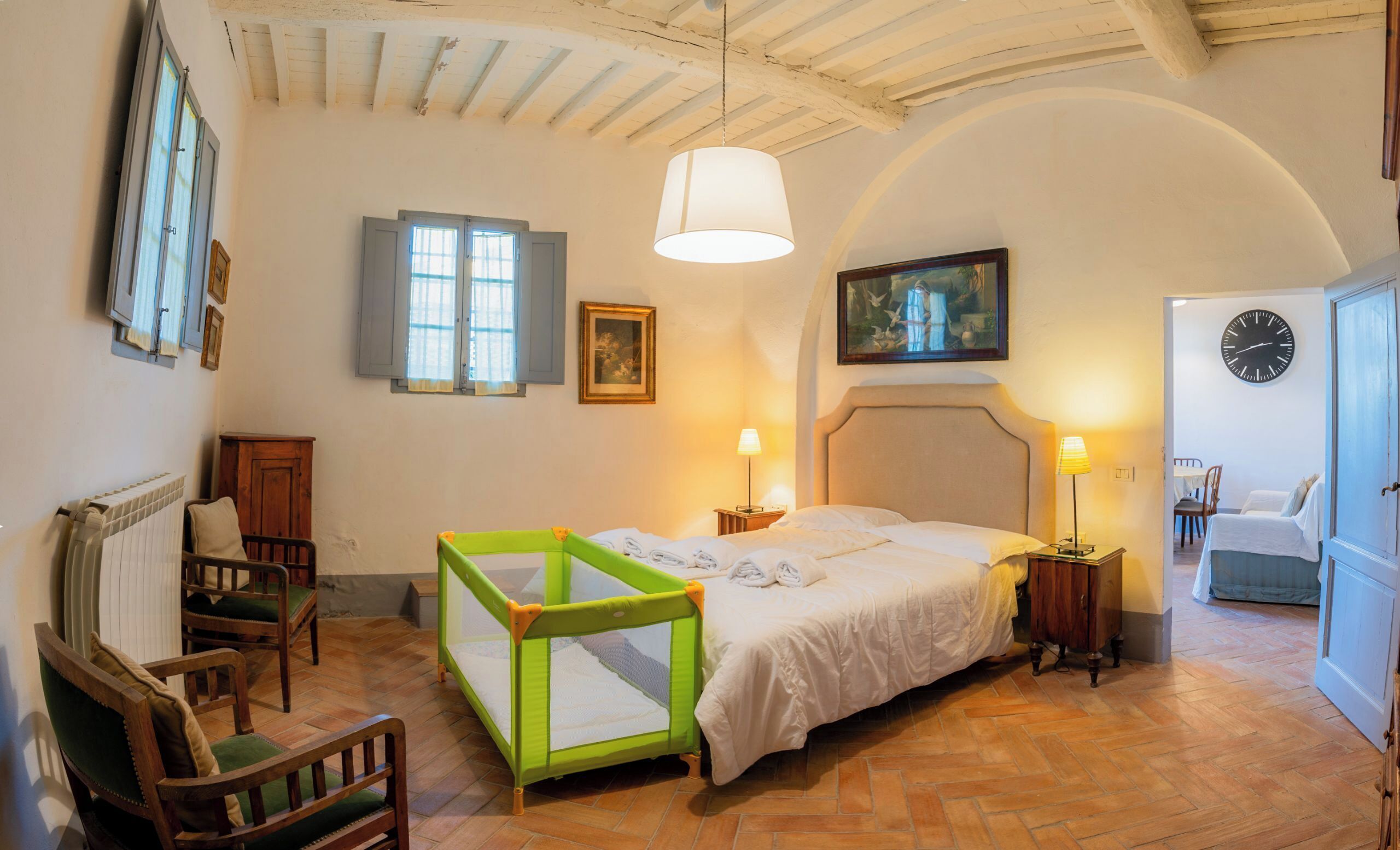 Un dormitorio con cama, una alberca para bebés, una silla de madera, un radiador, un reloj y una puerta.