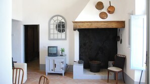 A room with a fireplace, a television on a cabinet, a chair, and a door. - Walnut – Tuscan 2 bedroom apartment on the ground floor with panoramic pool (Castelfiorentino)