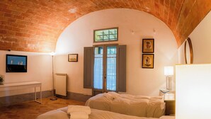 A bedroom with two beds, a radiator, a desk, and a TV on the wall. - Walnut – Tuscan 2 bedroom apartment on the ground floor with panoramic pool (Castelfiorentino)