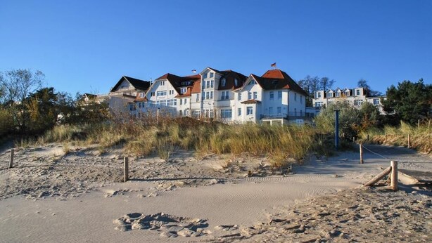A beachfront property with multiple buildings, a sandy beach, and sparse vegetation. - Promenandenhotel Admiral (Seebad Bansin)