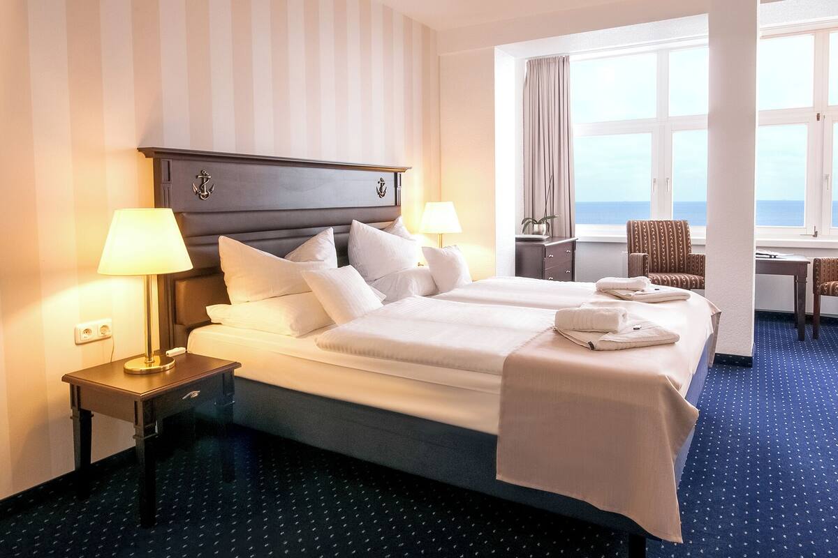 Une chambre d’hôtel avec un grand lit, deux lampes de chevet, un bureau et une vue sur la mer.