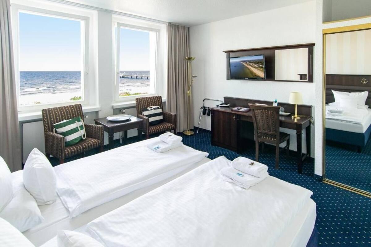 Une chambre d’hôtel avec deux lits, un bureau, une chaise, une télévision et une vue sur l’océan.